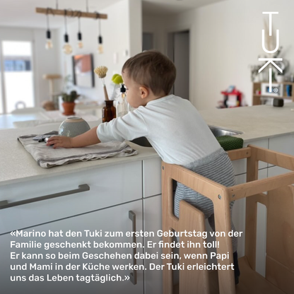 Kundenfoto: Kind steht im Tuki Lernturm an der Kuechenzeile, mit Zitat der Familie